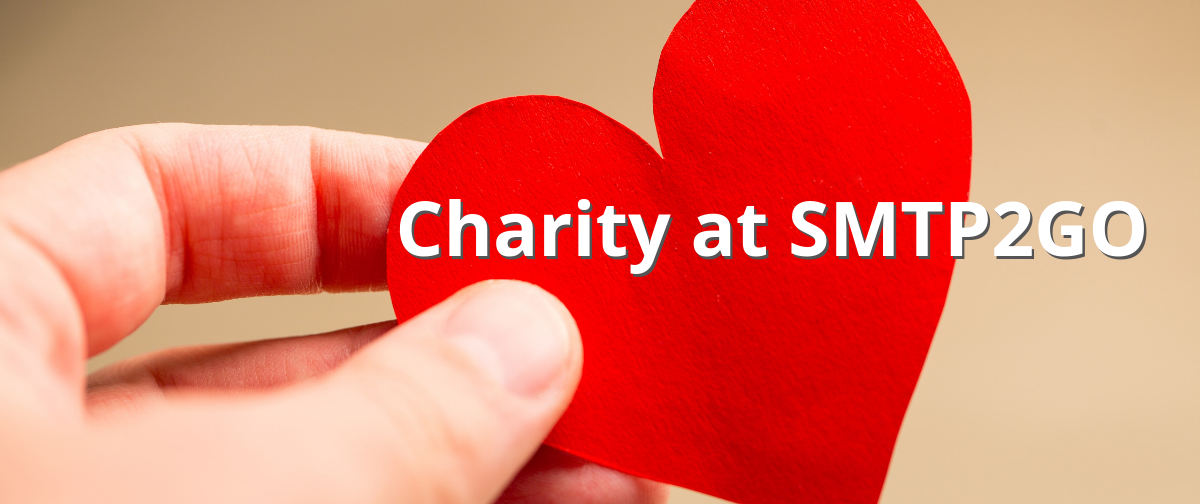a hand holding a red paper heart with the text "Charity at SMTP2GO"